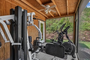 Une salle de sport équipée de matériel d’exercice, dotée d’un ventilateur de plafond et offrant une vue sur la verdure environnante.