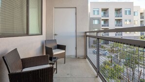 A balcony with wicker furniture, a closed door, and a view of adjacent buildings. - 2BR Tempe Oasis - King Beds, Pool, Gym, DT Tempe (Tempe)