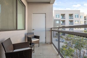 A balcony with wicker furniture, a closed door, and a view of adjacent buildings. - 2BR Tempe Oasis - King Beds, Pool, Gym, DT Tempe (Tempe)