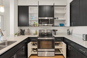 A modern kitchen with dark cabinetry, a stainless steel oven, and a microwave. - 2BR Tempe Oasis - King Beds, Pool, Gym, DT Tempe (Tempe)