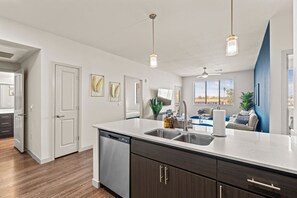 A modern kitchen with a dishwasher, double sink, and dark wood cabinets. - 2BR Tempe Oasis - King Beds, Pool, Gym, DT Tempe (Tempe)