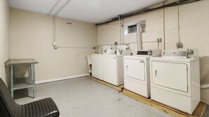 Une buanderie équipée de quatre machines à laver, d’une étagère en métal et d’un banc.