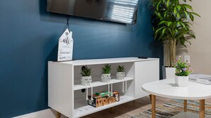 Un salon moderne avec un meuble de rangement blanc pour l’équipement audiovisuel, un téléviseur à écran plat fixé au mur, une plante en pot et une table basse ronde.