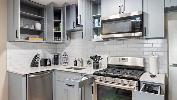Une cuisine moderne avec des meubles gris, un four à micro-ondes en acier inoxydable, une cuisinière à gaz et un lave-vaisselle.