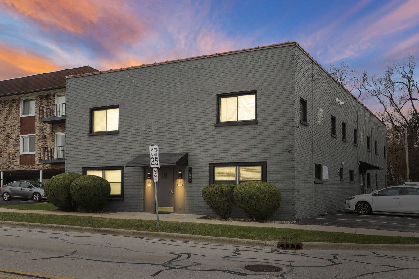 A modern two-story building with a speed limit sign, a garage entrance, and a well-maintained lawn.