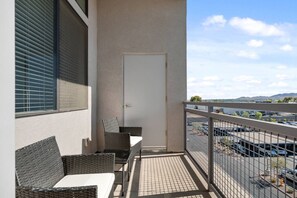 A balcony with wicker furniture, a door, and a view of a parking lot and mountains. - Luxe Desert Retreat - Pool, Hot Tub, Gym, Parking! (Tempe)