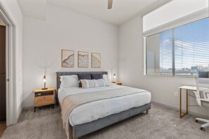 A bedroom with a bed, bedside tables, a desk, and a window with blinds. - Luxe Desert Retreat - Pool, Hot Tub, Gym, Parking! (Tempe)