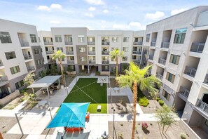 A multi-story residential building with balconies, a central courtyard with artificial grass, palm trees, and outdoor seating. - Tempe 2BR Escape | Pool, King Beds, Hot Tub, Gym (Tempe)