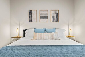Habitación de hotel con cama, dos mesitas de noche con lámparas y tres cuadros en la pared.