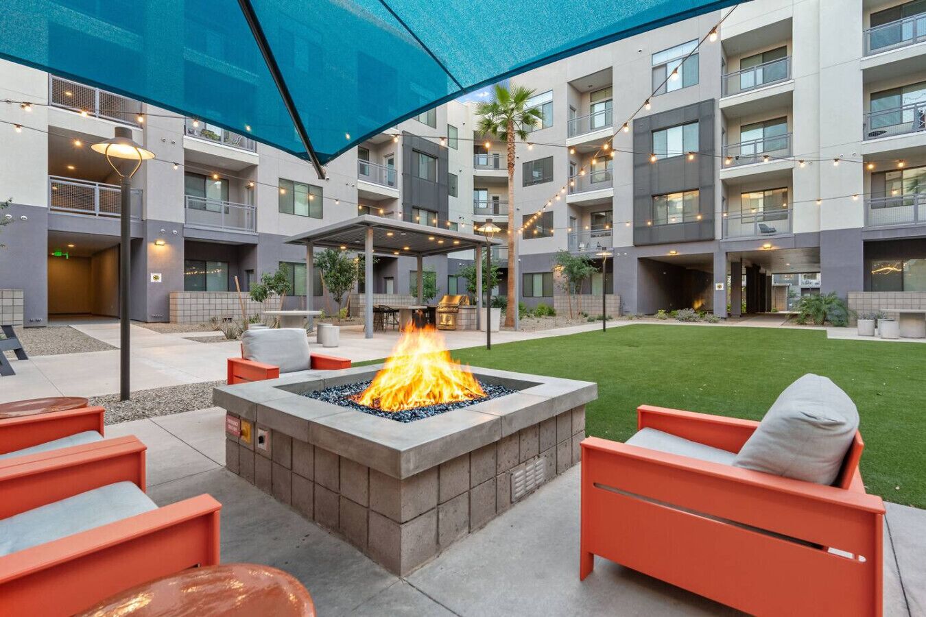A courtyard with a fire pit, outdoor seating, and a covered area with string lights.