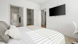 A bedroom with a bed, a TV, a wardrobe, and a bathroom visible through an open door. - 3BR Tempe Gem - Pool, King Beds, Gym, ASU Nearby (Tempe)