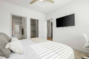 Quarto com cama, televisão, guarda-roupa e casa de banho visível por uma porta aberta.