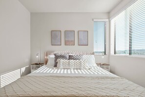 Quarto com cama, mesas de cabeceira e janela com persianas.