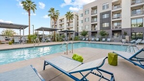 A pool area with lounge chairs and umbrellas, surrounded by a multi-story building with balconies. - 3BR Tempe Gem - Pool, King Beds, Gym, ASU Nearby (Tempe)