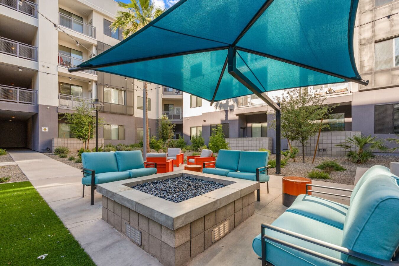 An outdoor seating area with a fire pit, lounge chairs, and a large umbrella.