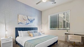 A bedroom with a bed, bedside tables, a desk, a chair, a window with blinds, and a ceiling fan. - Tempe`s Finest | King Beds, Pool & Prime Location! (Tempe)