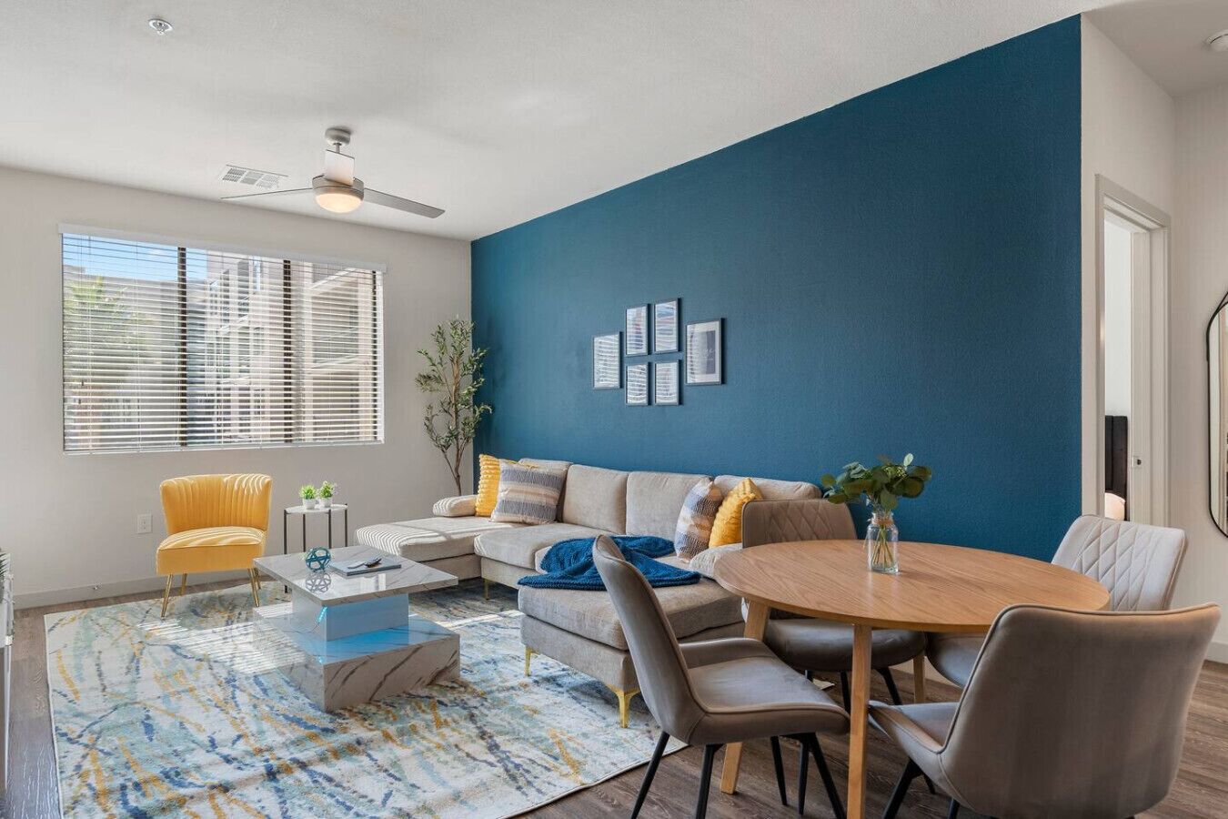 A modern living room with a blue accent wall, a sofa, a coffee table, and a dining area with chairs.