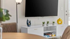 A modern living room with a flat-screen TV mounted on the wall, a white console table with decorative items, and a floor lamp. - Tempe`s Finest | King Beds, Pool & Prime Location! (Tempe)