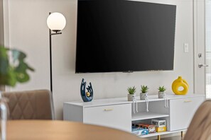 A modern living room with a flat-screen TV mounted on the wall, a white console table with decorative items, and a floor lamp. - Tempe`s Finest | King Beds, Pool & Prime Location! (Tempe)