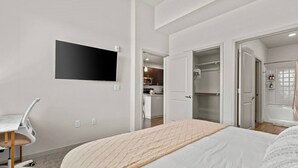 A modern hotel room with a bed, a desk, a TV, and a walk-in closet. - Sleek Desert Gem | Pool, Hot Tub, Gym, King Bed (Tempe)