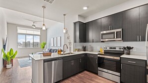 A modern kitchen with dark cabinets, stainless steel appliances, and a central island. - Sleek Desert Gem | Pool, Hot Tub, Gym, King Bed (Tempe)