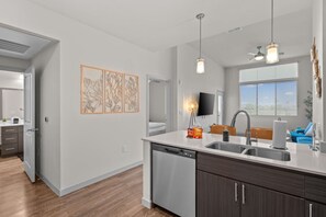 Eine moderne Küche mit Geschirrspüler, Spüle und einer Arbeitsplatte. Ein Fernseher ist an der Wand befestigt und es gibt ein Fenster mit Jalousien.