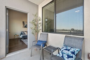 Ein modernes Wohnzimmer mit einer Couch, Sesseln, einem kleinen Tisch und einem großen Fenster mit Jalousien.