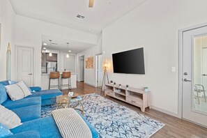 Un salón moderno con un sofá azul, una mesa de centro y un televisor montado en la pared.