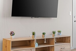 Una consola de madera con un televisor de pantalla plana montado encima, y cuatro macetas con plantas que tienen caras caricaturescas.