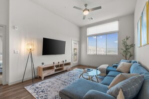 A modern living room with a flat-screen TV, a ceiling fan, a sofa set, a coffee table, and a floor lamp. - Chic 1BR - Mountain Views, Pool, Hot Tub, King Bed (Tempe)