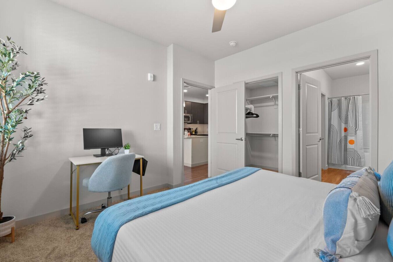 A bedroom with a bed, a desk with a computer, a chair, a potted plant, and a walk-in closet.