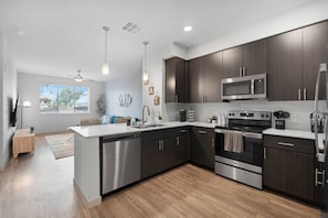 A modern kitchen with dark wood cabinets, stainless steel appliances, and a central island. - Rest & Recover - King Bed, Pool, Gym & More (Tempe)