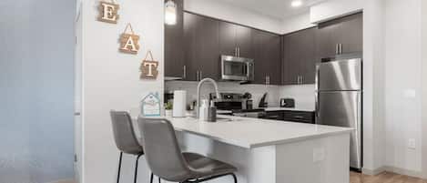 Uma cozinha moderna com uma ilha central, banquetas, micro-ondas, frigorífico e decorações de parede em madeira.