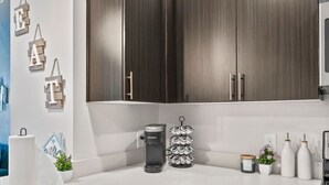 Une cuisine moderne avec des meubles de couleur bois foncé, un plan de travail blanc, une machine à café Keurig, un distributeur d’essuie-tout et une pile de dosettes de café.