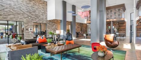 Eine geräumige Lobby mit modernem Design, inklusive Backsteinwand, großer Säulen und verschiedenen Sitzgelegenheiten wie Sofas und Sessel.