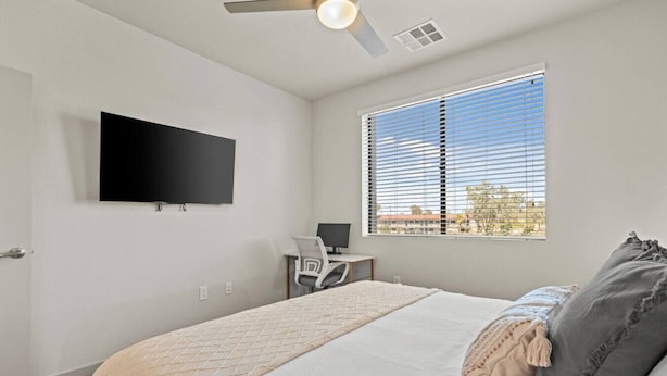 A bedroom with a bed, a desk with a computer, a TV on the wall, and a window with blinds. - Tempe Oasis | King Beds, Pool, Gym, DT Tempe & ASU (Tempe)