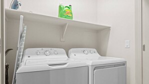 A laundry area with a front-loading washer and dryer, a drying rack, and a shelf with cleaning products. - Tempe Oasis | King Beds, Pool, Gym, DT Tempe & ASU (Tempe)