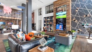 A modern hotel lobby with a leather sofa, a coffee table, a TV mounted on a wooden wall, and a bull statue. - Tempe Oasis | King Beds, Pool, Gym, DT Tempe & ASU (Tempe)