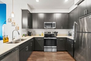 A modern kitchen with dark cabinetry, stainless steel appliances, a double sink, and a wooden floor. - Luxury Tempe 1BR | Pool, Hot Tub, Gym, King Bed (Tempe)