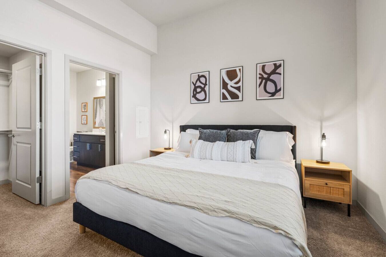 A bedroom with a large bed, bedside tables, and abstract wall art.