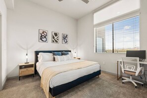A bedroom with a bed, bedside tables, a desk with a chair, and a window with blinds. - Luxury Tempe 1BR | Pool, Hot Tub, Gym, King Bed (Tempe)