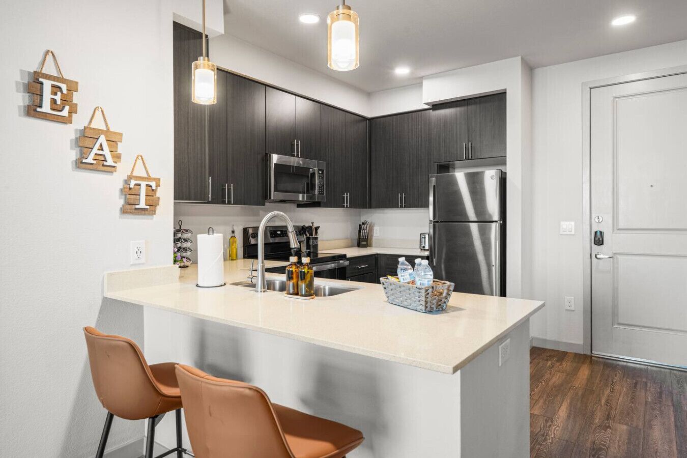 A modern kitchen with dark cabinets, stainless steel appliances, a central island with seating, and pendant lighting.