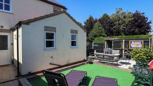 A house with a patio area featuring two chairs and a table, a small deck, and a sign advertising a product.