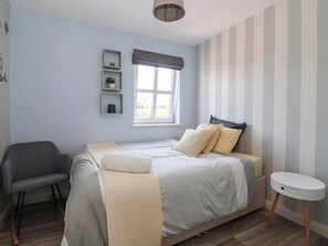 A bedroom with a bed, bedside table, chair, and a window with curtains. - 3 Mill Lane (Grimsby)