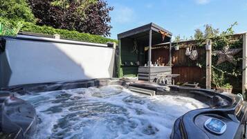 Un bain à remous doté d’un panneau de commande, entouré d’une clôture en bois et de verdure.