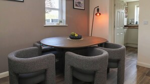 A dining area with a round table, four chairs, a pendant light, and framed pictures on the wall.