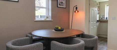 Un comedor con una mesa redonda, cuatro sillas, una lámpara colgante y cuadros en la pared.