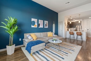 A modern living room with a sofa, coffee table, and a large plant. - 1BR Tempe Haven - King Bed, Pool, Hot Tub, Gym (Tempe)