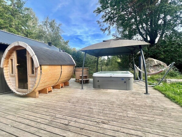 A wooden deck with a sauna, a hot tub, and a covered seating area.