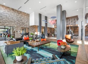 Eine geräumige Lobby mit modernem Design, inklusive Backsteinwand, großer Säulen und verschiedenen Sitzgelegenheiten wie Sofas und Sessel.